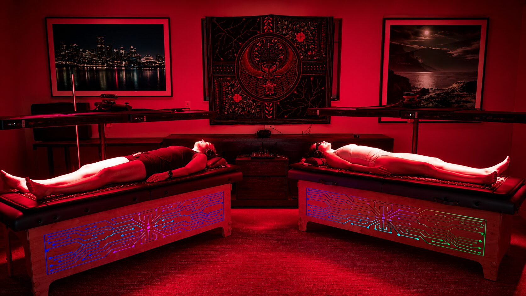 Two people lying side by side on Vibro Vessels during a session, bathed in red light